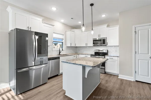 a kitchen with kitchen island granite countertop a refrigerator a sink dishwasher a stove and a oven with wooden floor