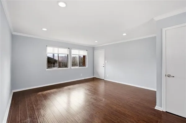 an empty room with wooden floor kitchen view and a window