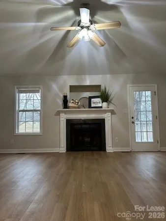 a view of an empty room with wooden floor fireplace and a window