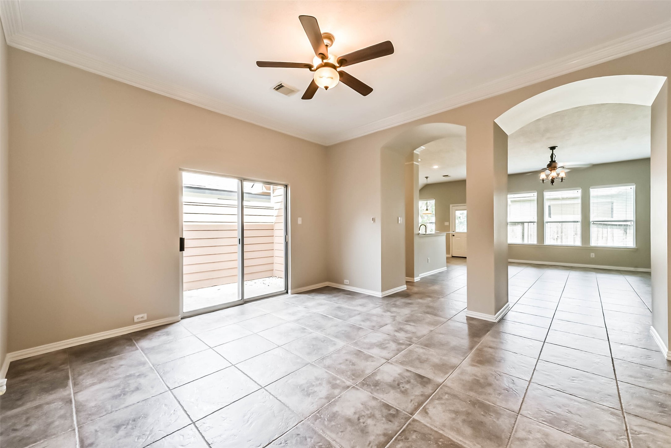 30910 Blue Ridge Park Lane Spring, TX 77386 - Photo 19 of 50 Bright and spacious living area featuring elegant tile flooring, a ceiling fan, and sliding glass doors that open to a private outdoor space. An arched entryway leads to a well-lit dining area with multiple windows.