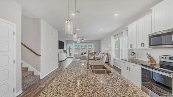 a large white kitchen with stainless steel appliances granite countertop a stove a sink dishwasher a refrigerator white cabinets and wooden floor