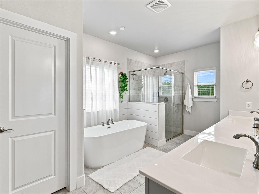 10216 Finch Road Sanger, TX 76266 - Photo 18 of 40 Freestanding soaking tub, glass-enclosed shower with tile surround, dual vanity with undermount sinks, and windows providing natural light