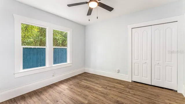 an empty room with wooden floor chandelier fan and windows