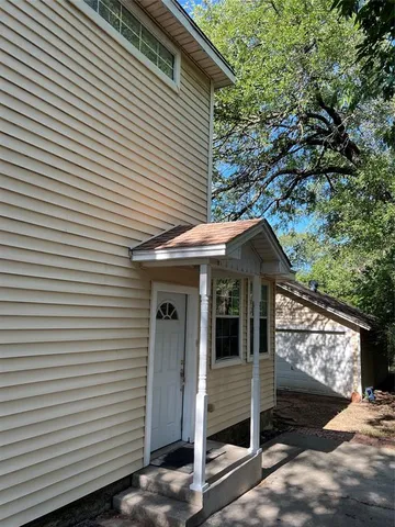 a view of a white house with a large tree and wooden fence