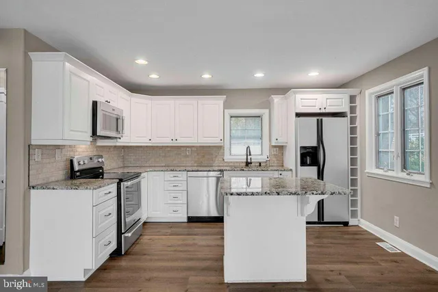 a large kitchen with stainless steel appliances granite countertop a stove top oven a sink dishwasher and a refrigerator with wooden floor