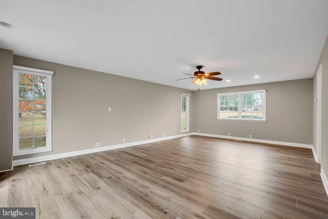 an empty room with wooden floor chandelier fan and windows