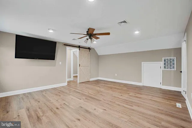 a view of an empty room with wooden floor and a ceiling fan