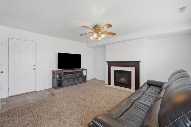 5576 South 4100th Street West Roy, UT 84067 - Photo 15 of 35 Living area featuring a gas fireplace with a dark wood mantel and white surround, complemented by a ceiling fan with integrated lighting, and carpet flooring