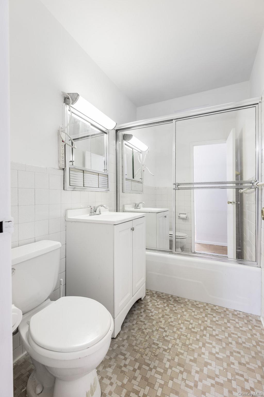 40 Brighton 1st Road, Unit 3J Brooklyn, NY 11235 - Photo 11 of 23 Full bathroom with vanity, toilet, tile walls, and bath / shower combo with glass door