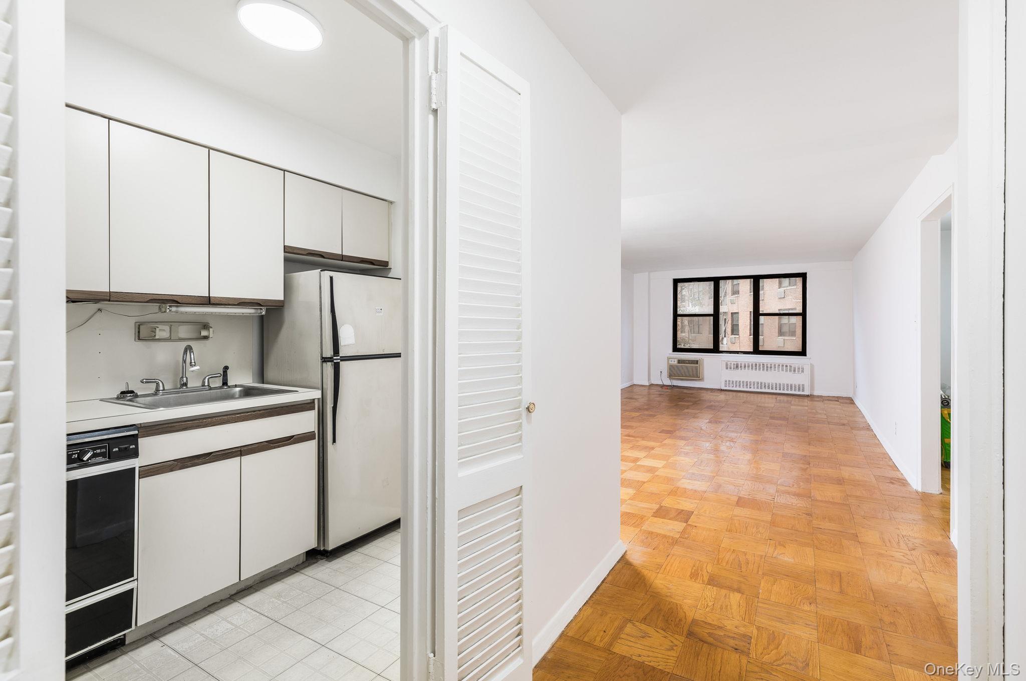 40 Brighton 1st Road, Unit 3J Brooklyn, NY 11235 - Photo 4 of 23 Kitchen with radiator, white cabinetry, sink, white refrigerator, and light parquet flooring