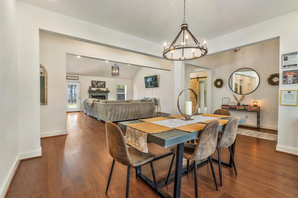 1909 Willowcrest Loop Denton, TX 76205 - Photo 6 of 40 Dining space featuring dark wood finished floors, a barn door, vaulted ceiling, a fireplace, and a chandelier