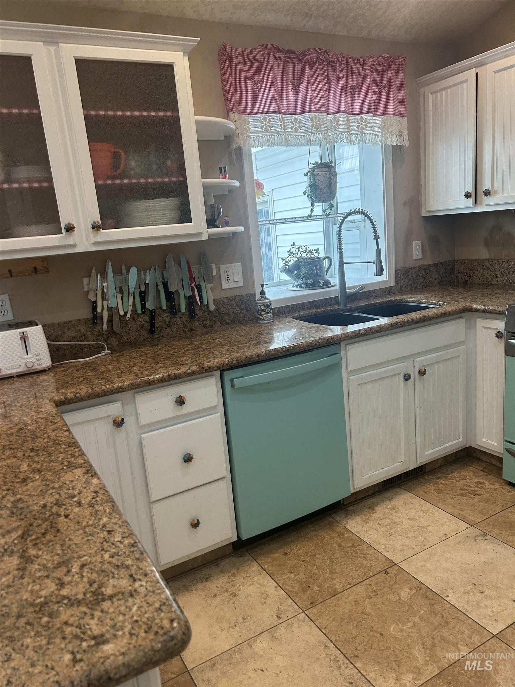 1444 East Doberman Street Meridian, ID 83642 - Photo 7 of 31 Kitchen featuring white cabinetry with some glass-front doors, granite countertops, an undermount double basin sink with a high-arc faucet, a contrasting dishwasher, and tiled flooring
