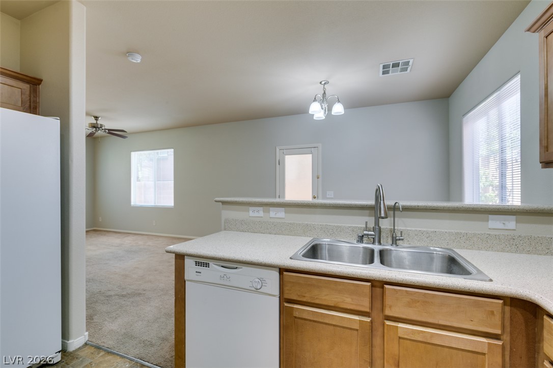 8937 Caledon Ridge Court Las Vegas, NV 89149 - Photo 26 of 43 A functional kitchen with a double sink and light wood cabinetry overlooks the adjacent living area.