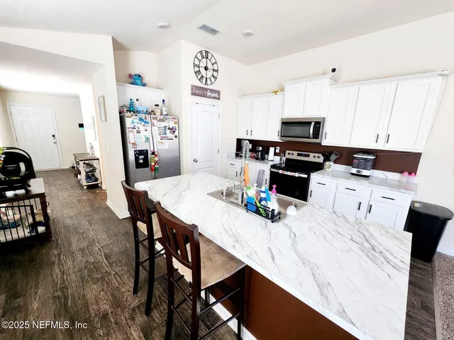 a kitchen with stainless steel appliances kitchen island granite countertop a table chairs and a refrigerator