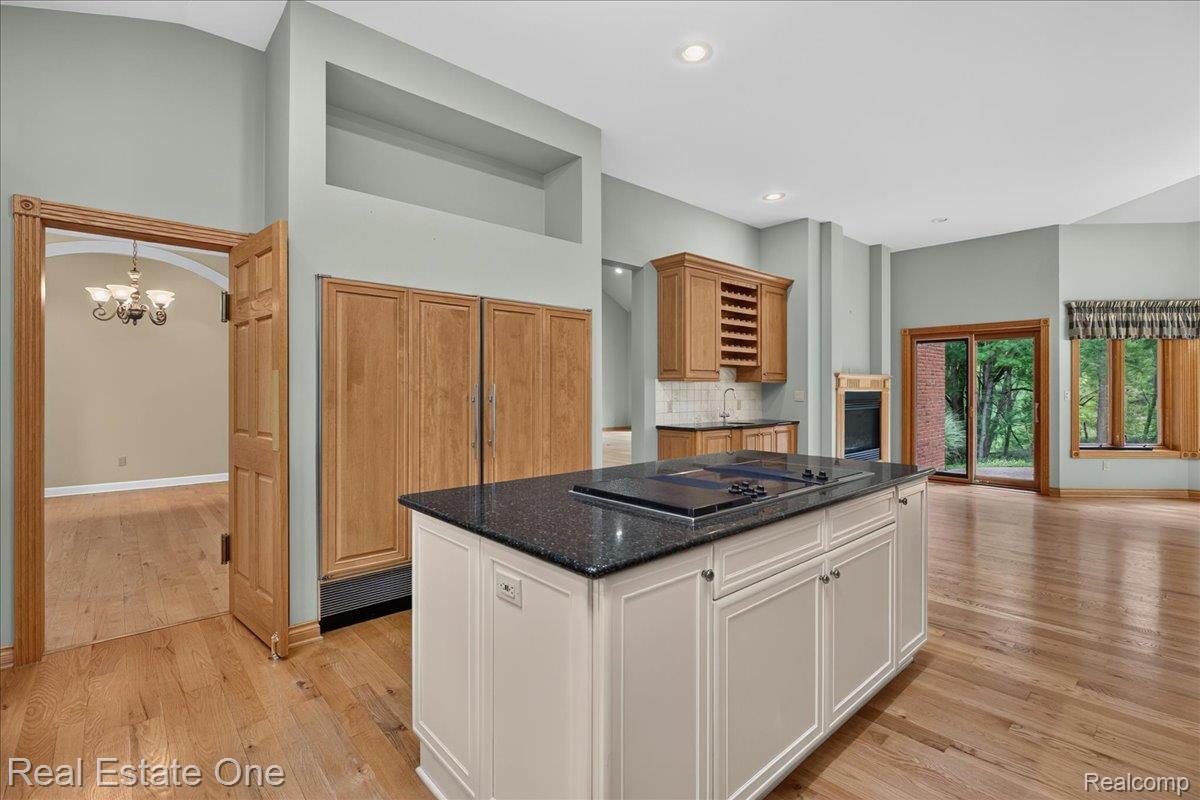 425 Courtney Road Leonard, MI 48367 - Photo 20 of 89 Kitchen featuring an island with a built-in cooktop and dark stone countertop, light wood-finish flooring, a built-in refrigerator with wood paneling, a wet bar with integrated wine storage, and a sliding glass door to exterior