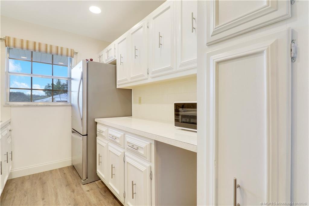 211 Manatee Lane, Unit D Fort Pierce, FL 34982 - Photo 11 of 25 a kitchen with stainless steel appliances a refrigerator a stove and white cabinets with wooden floor