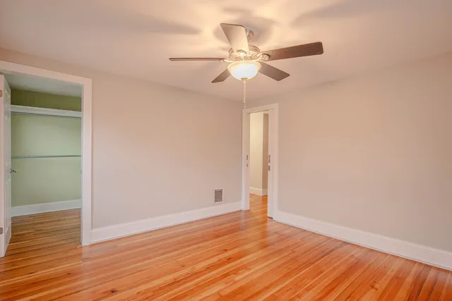 an empty room with wooden floor fan and windows
