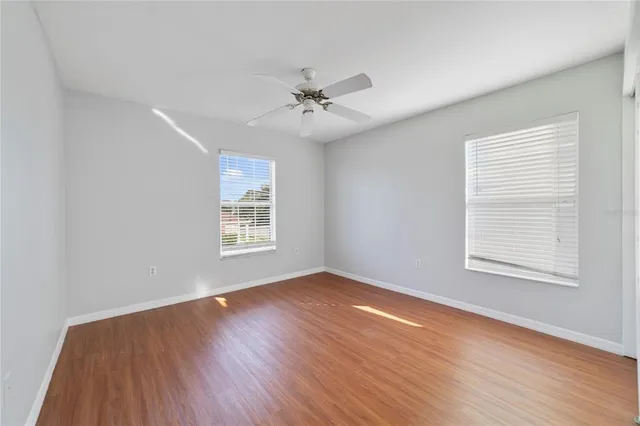 an empty room with wooden floor ceiling fan and windows