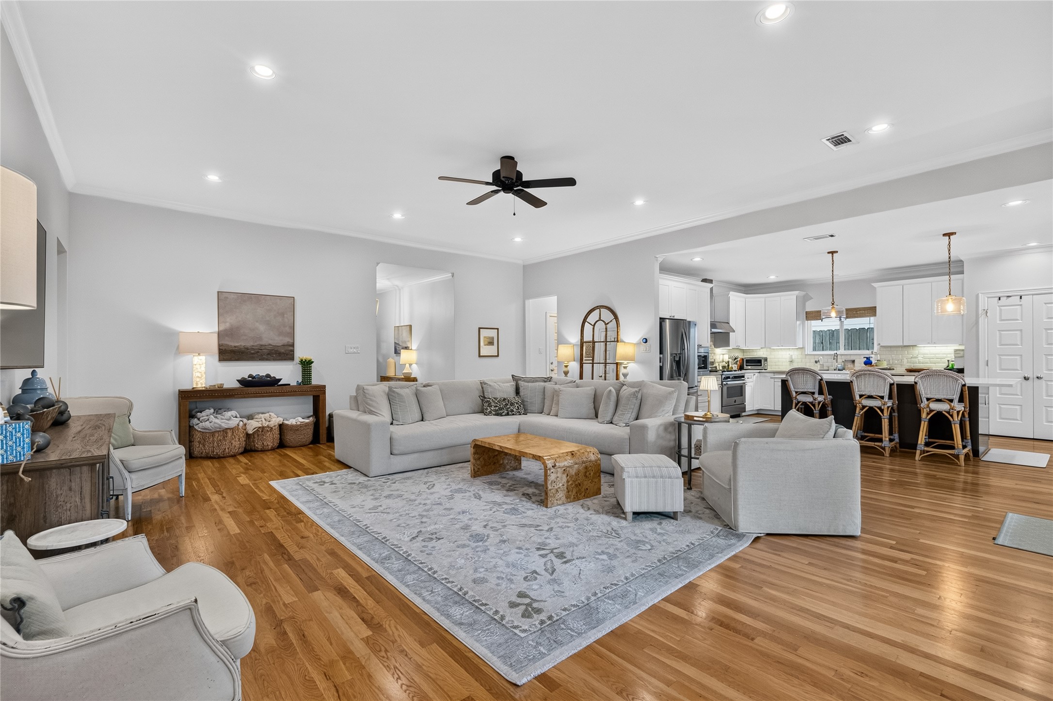 Spacious open-concept living area featuring hardwood floors, a cozy sectional sofa, and a modern kitchen with a large island and pendant lighting, perfect for entertaining.