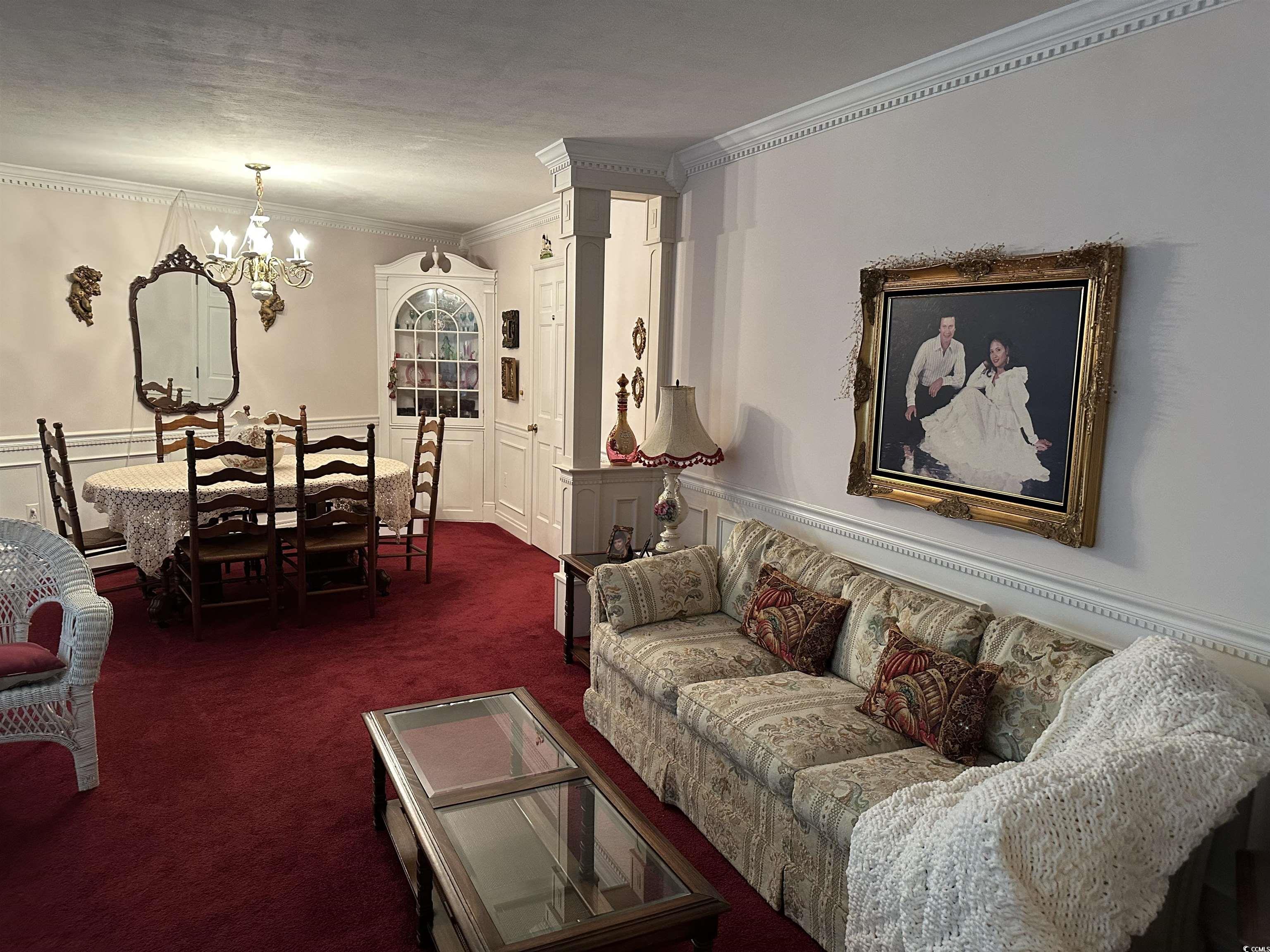 2840 Pennyroyal Road Georgetown, SC 29440 - Photo 21 of 36 Living area featuring ornamental molding, a wainscoted wall, dark carpet, a decorative wall, and a chandelier