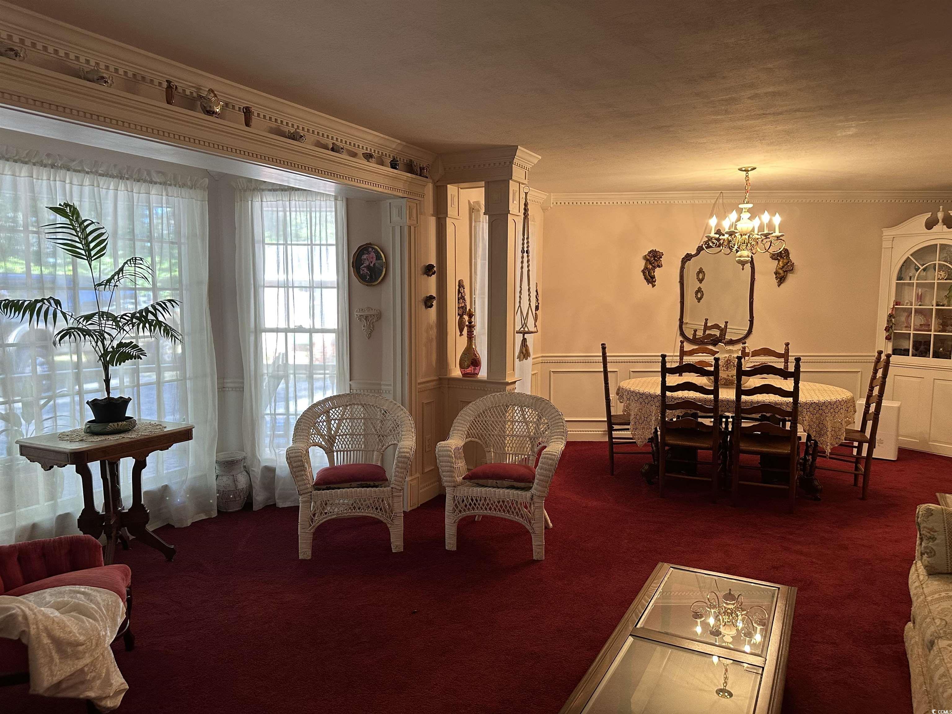 2840 Pennyroyal Road Georgetown, SC 29440 - Photo 22 of 36 Carpeted living room featuring ornamental molding, a decorative wall, a chandelier, and a wainscoted wall