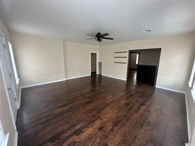 an empty room with wooden floor ceiling fan and window