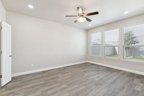 an empty room with wooden floor chandelier fan and windows