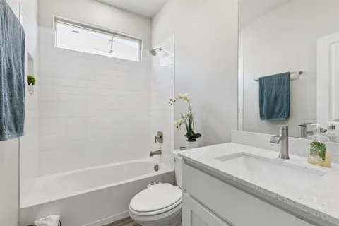 a bathroom with a granite countertop bathtub shower sink vanity mirror and toilet