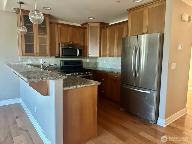 a kitchen with stainless steel appliances granite countertop a refrigerator a stove and a sink with wooden floor