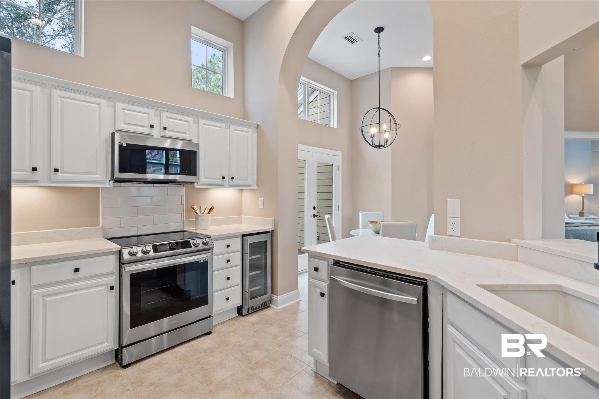 9259 Genipa Way Gulf Shores, AL 36542 - Photo 16 of 72 Kitchen featuring appliances with stainless steel finishes, white cabinetry, light stone countertops, decorative light fixtures, and beverage cooler
