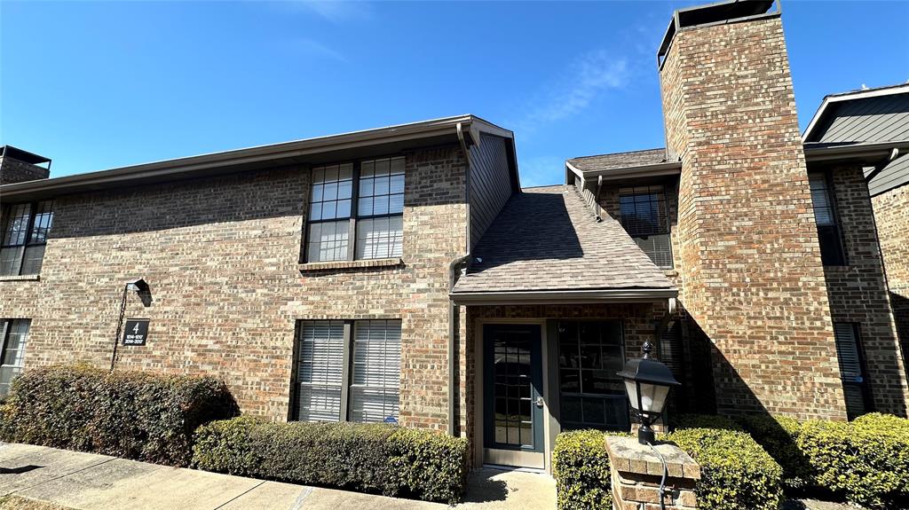 View of front of home with roof with shingles, a chimney, and brick siding