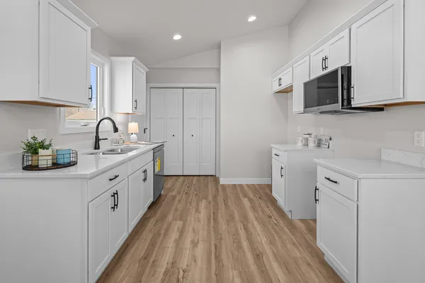 a kitchen with granite countertop a sink dishwasher stove and white cabinets with wooden floor