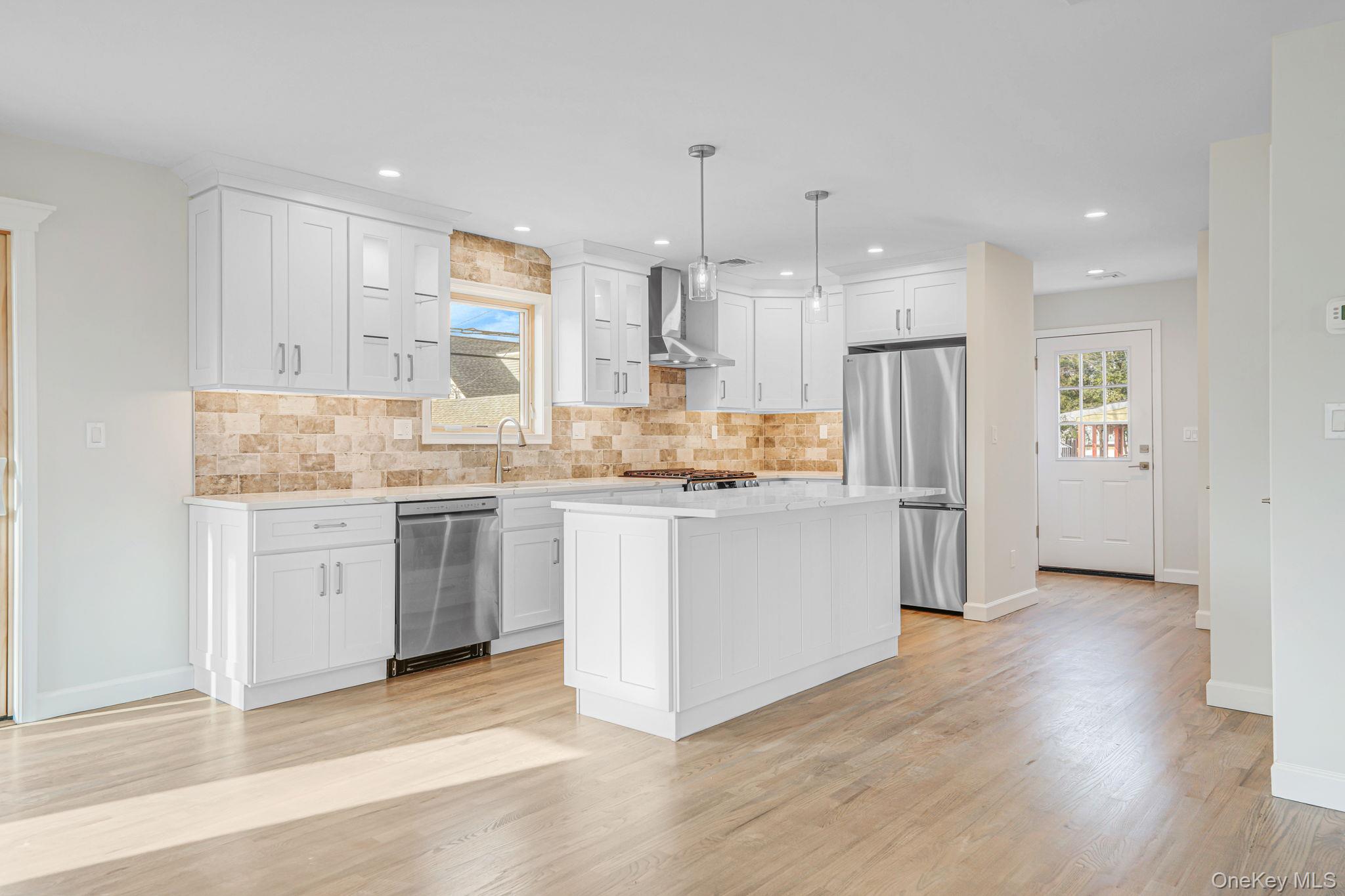 115 Riviera Parkway Lindenhurst, NY 11757 - Photo 26 of 33 Kitchen featuring white cabinetry, a center island, decorative light fixtures, stainless steel appliances, and light wood-style flooring