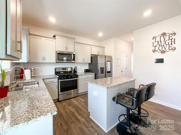 a kitchen with granite countertop a stove top oven a sink dishwasher and a refrigerator with wooden floor