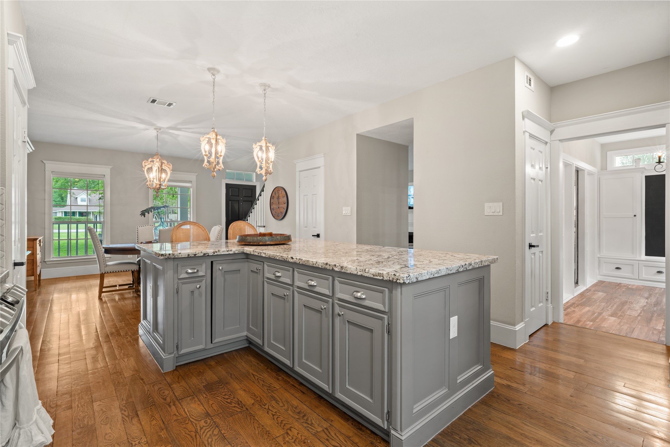 36 Wind River Drive Conroe, TX 77384 - Photo 21 of 45 The photo showcases a bright, open kitchen and dining area with hardwood floors. It features a large, granite-topped island with gray cabinetry, elegant pendant lighting, and a view into a cozy dining space. There's ample natural light from large windows, creating an inviting atmosphere.