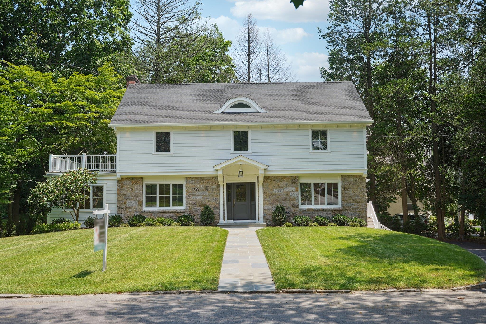 Colonial home with stone siding, a front yard, and a shingled roof