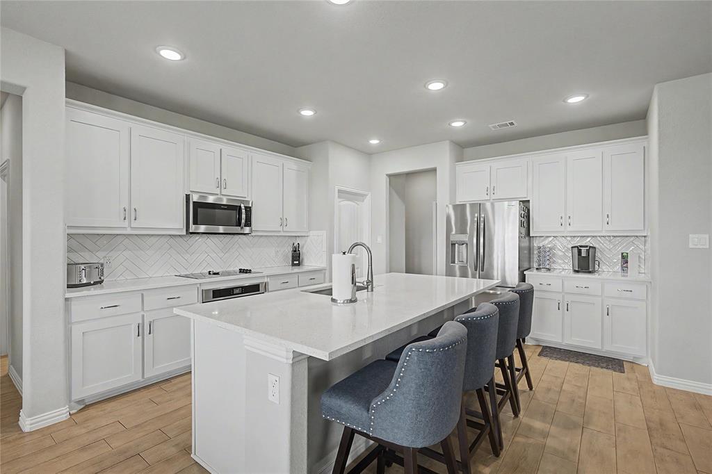 185 Chester Road Springtown, TX 76082 - Photo 17 of 40 Kitchen featuring light wood-finish flooring, white cabinetry, integrated stainless steel appliances, a herringbone tile backsplash, and a large central island with a solid surface countertop
