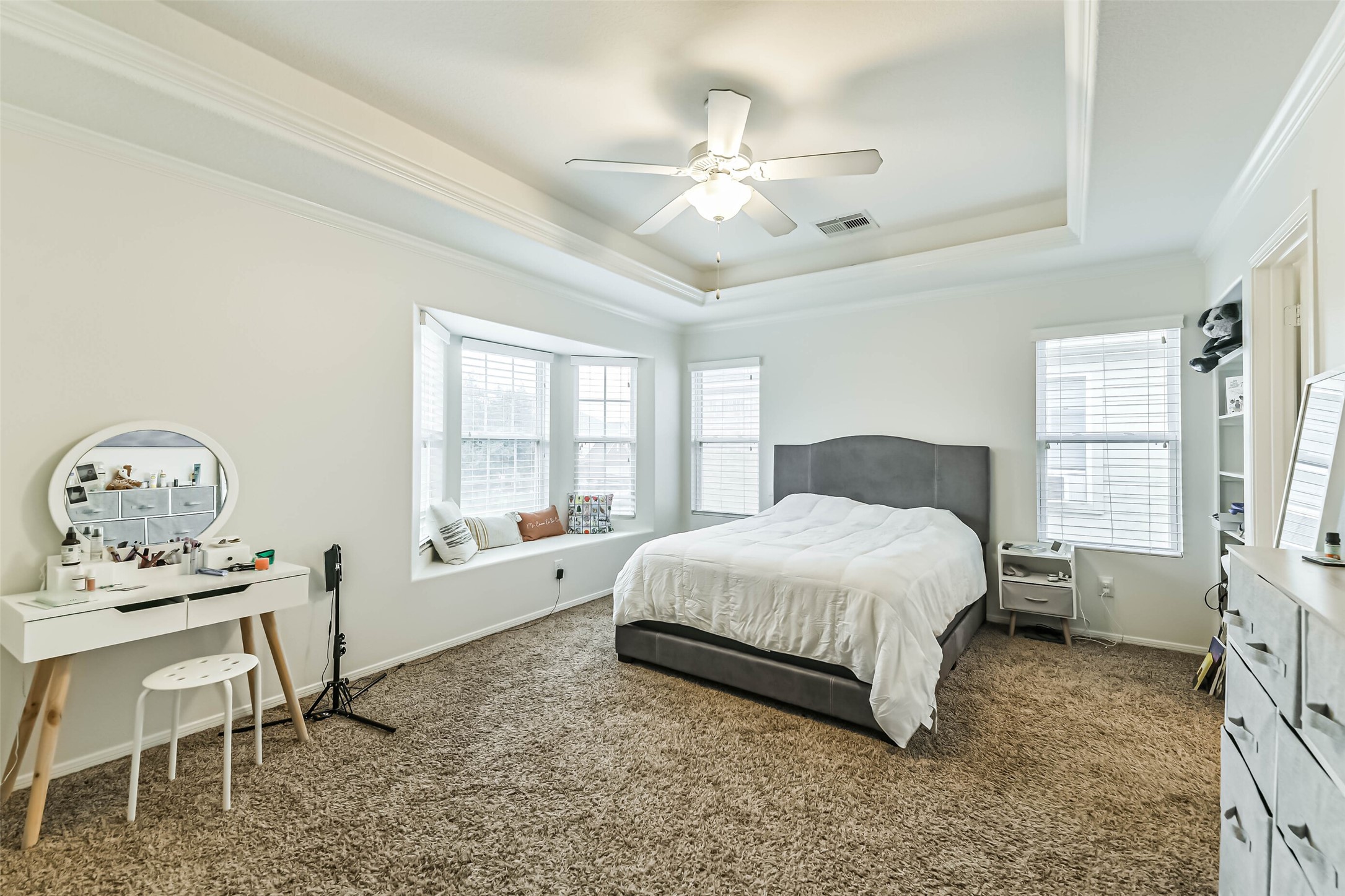 22538 Goss Spring Court Spring, TX 77373 - Photo 23 of 36 Spacious bedroom with a cozy carpet, featuring a large bed, tray ceiling, and ample natural light from multiple windows. Includes a vanity area and a comfortable window seat for relaxation.