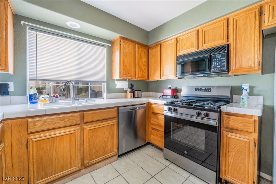 1851 Hillpointe Road, Unit 2912 Henderson, NV 89074 - Photo 6 of 28 Kitchen with tile countertops, light tile patterned flooring, a sink, appliances with stainless steel finishes, and brown cabinetry