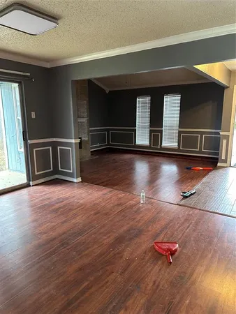 an empty room with wooden floor kitchen view and a window