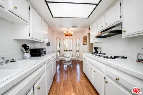 a kitchen with stainless steel appliances a stove a sink dishwasher and white cabinets with wooden floor