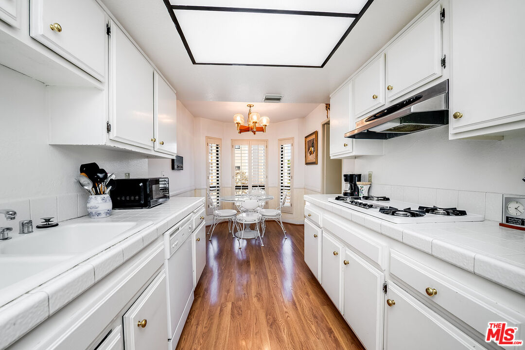 10409 Riverside Drive, Unit 203 Toluca Lake, CA 91602 - Photo 14 of 34 a kitchen with stainless steel appliances a stove a sink dishwasher and white cabinets with wooden floor