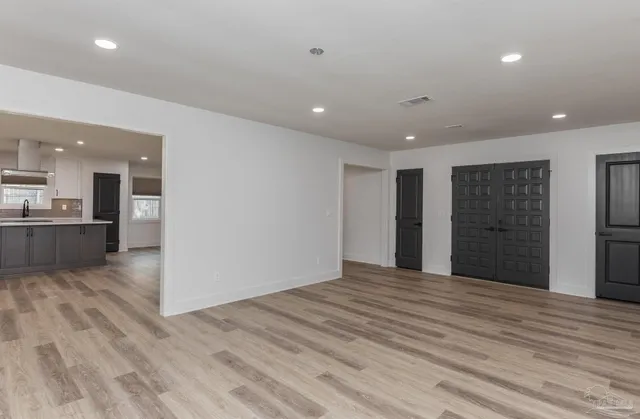 a view of an empty room with wooden floor and a kitchen
