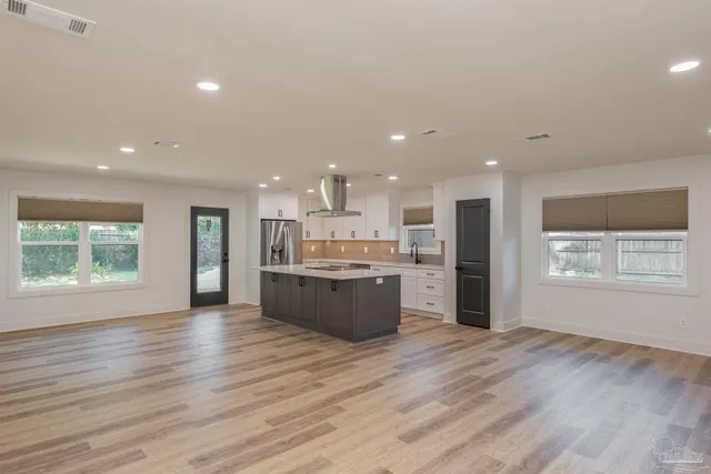 a large kitchen with stainless steel appliances granite countertop a large counter top a wooden floors and a large window