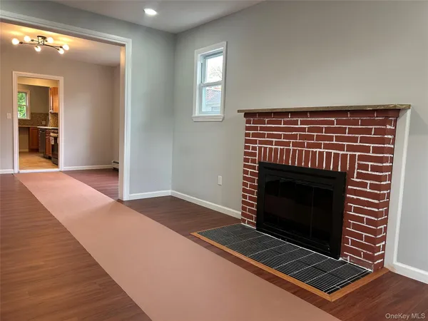 a view of an empty room with wooden floor fireplace and a window