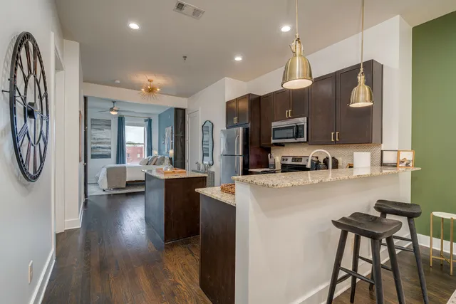 a kitchen with stainless steel appliances kitchen island granite countertop a refrigerator a stove top oven a sink dishwasher and white cabinets with wooden floor