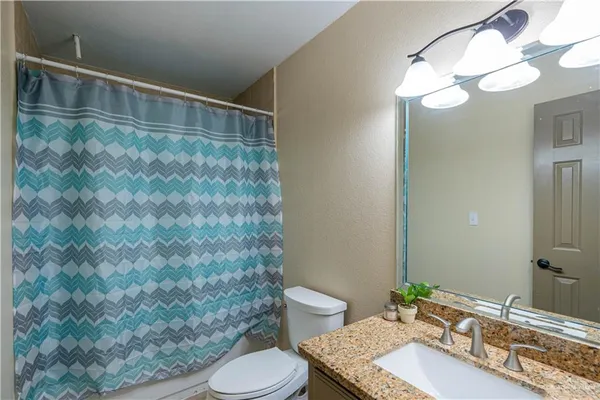 a bathroom with a granite countertop sink a toilet a mirror and shower curtain