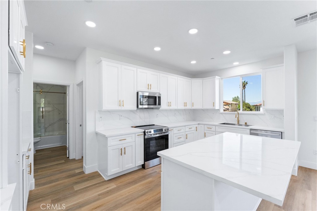 1981 Lyon Avenue Riverside, CA 92503 - Photo 13 of 58 a large white kitchen with stainless steel appliances granite countertop a stove a sink a refrigerator and white cabinets with wooden floor