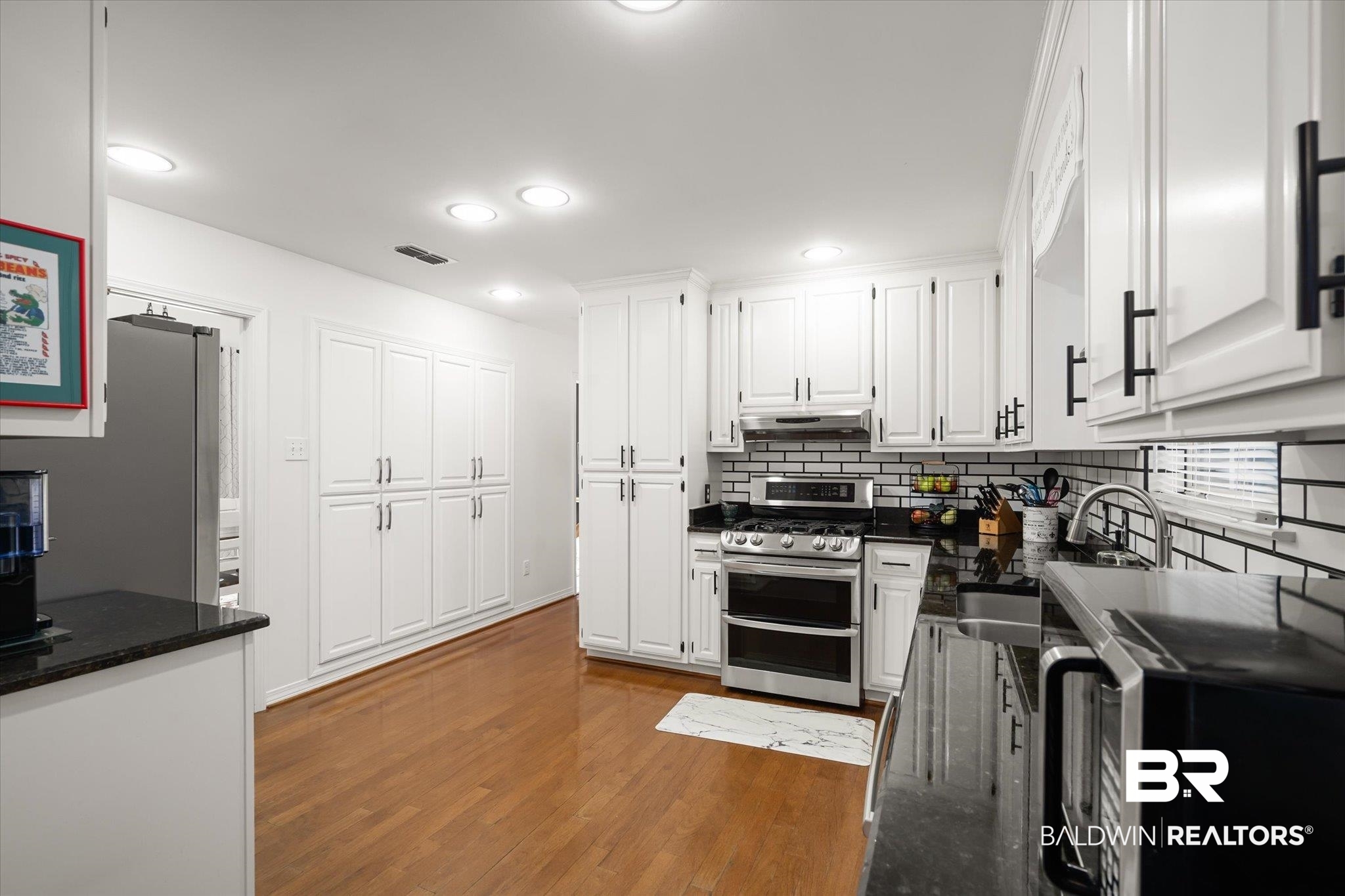 19924 Hunters Loop Fairhope, AL 36532 - Photo 9 of 40 Kitchen with decorative backsplash, dark stone counters, hardwood / wood-style flooring, stainless steel range oven, and white cabinetry