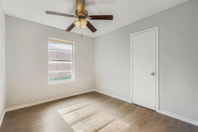 an empty room with wooden floor ceiling fan and windows